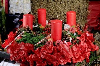 four red candles arranged on greenery and red paper, decorated with candy canes, fir cones and roses