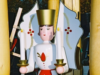 shaped, painted, wooden figure in white, red robe with big wings and two candles in the hand