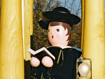 shaped, painted wooden figure with black robe, hat and open book.
