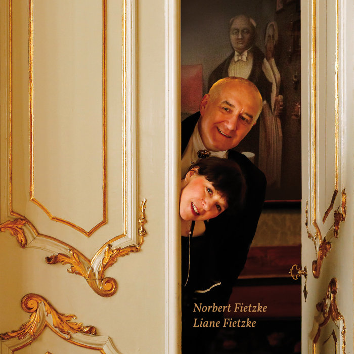 Duo "con emozione": Liane Fietzke, Gesang/Moderation, Norbert Fietzke, Piano Zwei Personen schauen durch eine prächtige Tür.