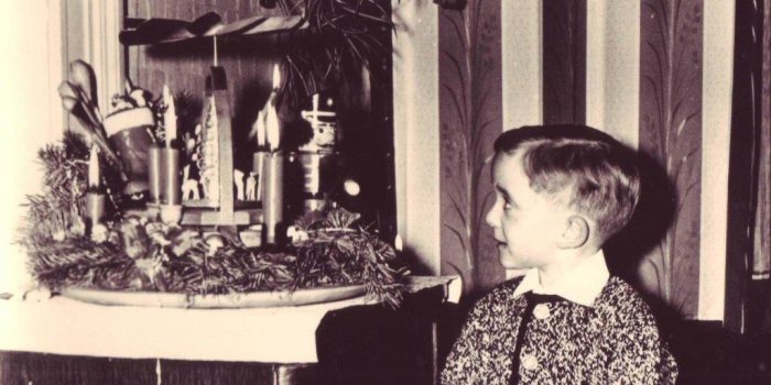 Kleiner Junge mit Strickjacke schaut auf Adventskranz.