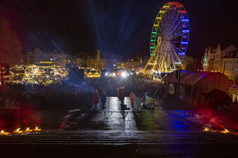Blick von den Domstufen auf den abendlichen Erfurter Weihnachtsmarkt, auf der Bühne mehrere Menschen