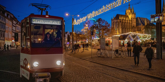 Eine Straßenbahn neben dem beleuchteten Eingang zum Erfurter Weihnachtsmarkt
