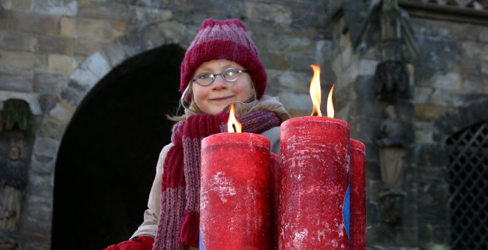 Ein Mädchen hat die großen roten Kerzen am Adventskranz auf den Domstufen angezündet.