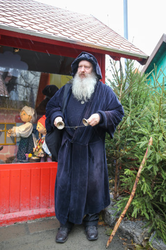 Mann mit weißem Bart und langem dunklem Umhang steht vor der Märchenhütte und sprcht.