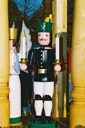 gedrechselte, bemalte Holzfigur mit schwarz-weißer Uniform und Kerzen in der Hand
